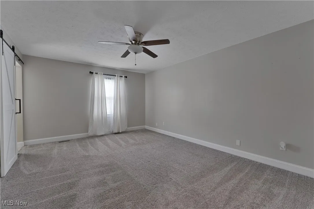 Empty room with a barn door, ceiling fan, a textured ceiling, and light carpet