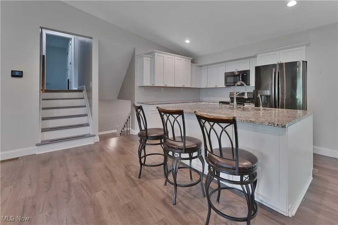 Kitchen with stainless steel appliances, lofted ceiling, white cabinets, light stone countertops, and a kitchen island with sink