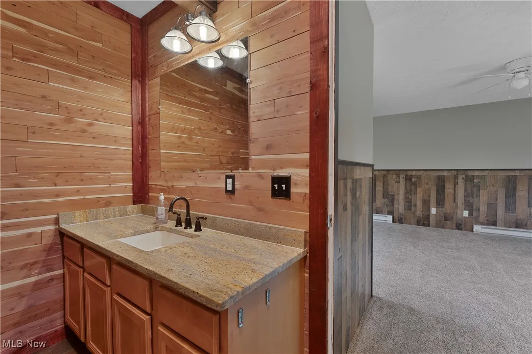 Bathroom with wood walls, a ceiling fan, and vanity