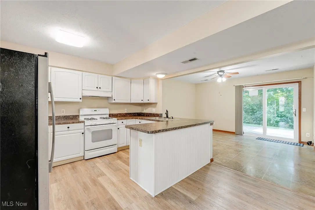 Kitchen with freestanding refrigerator, white range with gas cooktop, a peninsula, dark countertops, and under cabinet range hood
