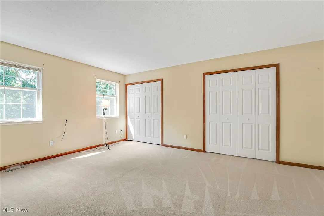 Unfurnished bedroom with two closets, multiple windows, and light colored carpet