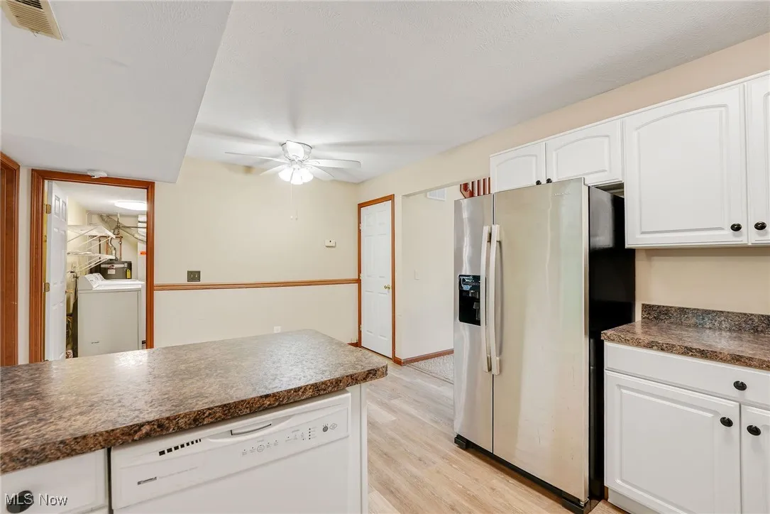 Kitchen with stainless steel fridge with ice dispenser, white dishwasher, dark countertops, a ceiling fan, and white cabinets