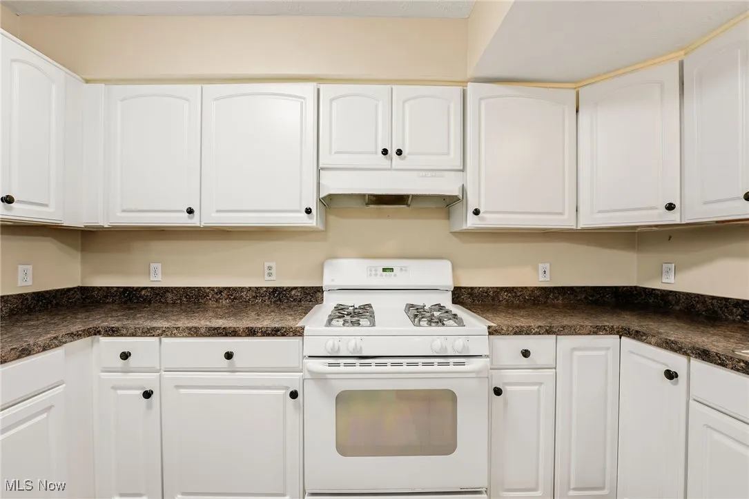 Kitchen featuring white range with gas stovetop, under cabinet range hood, and dark countertops