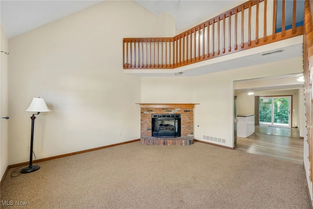 Unfurnished living room featuring carpet flooring, high vaulted ceiling, and a brick fireplace