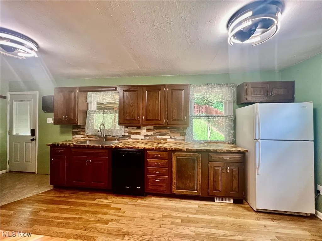 Kitchen with freestanding refrigerator, dishwasher, light wood-style flooring, decorative backsplash, and a textured ceiling