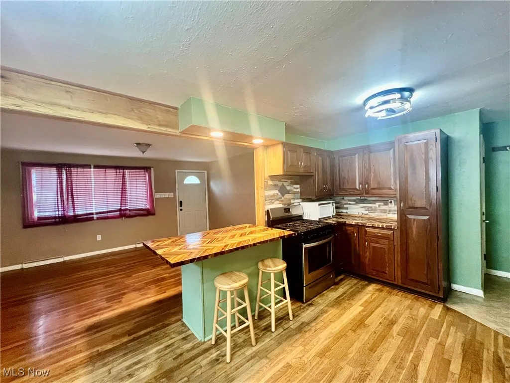 Kitchen featuring stainless steel gas range oven, butcher block counters, white microwave, light wood-style floors, and a textured ceiling