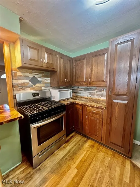Kitchen featuring stainless steel range with gas cooktop, white microwave, light wood-type flooring, and butcher block counters