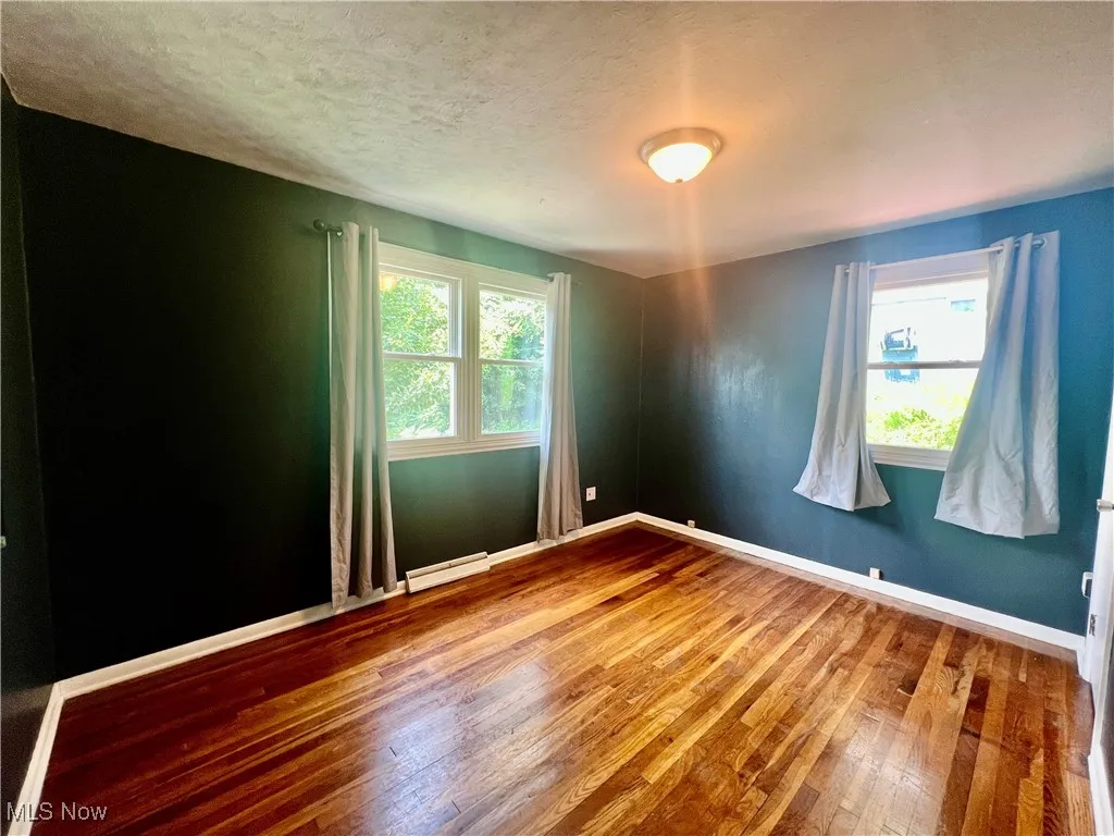 Empty room with hardwood / wood-style floors, a textured ceiling, and a baseboard radiator