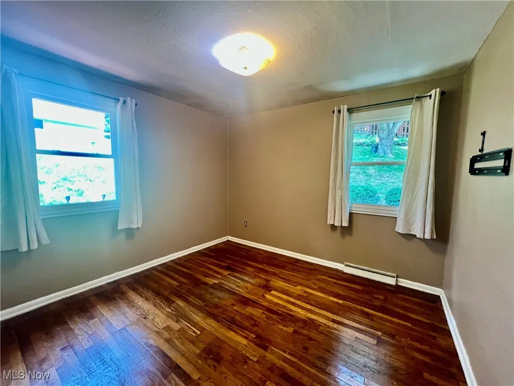 Unfurnished room with hardwood / wood-style floors and a baseboard heating unit