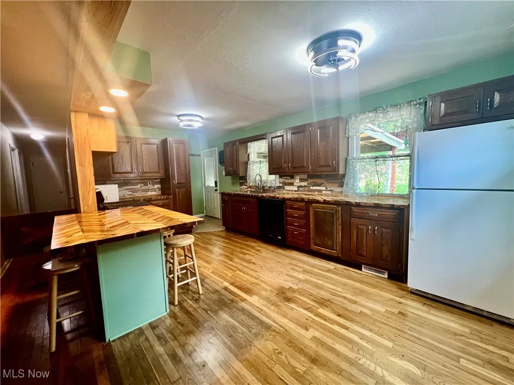 Kitchen featuring freestanding refrigerator, wooden counters, dishwasher, a breakfast bar, and light wood-style flooring