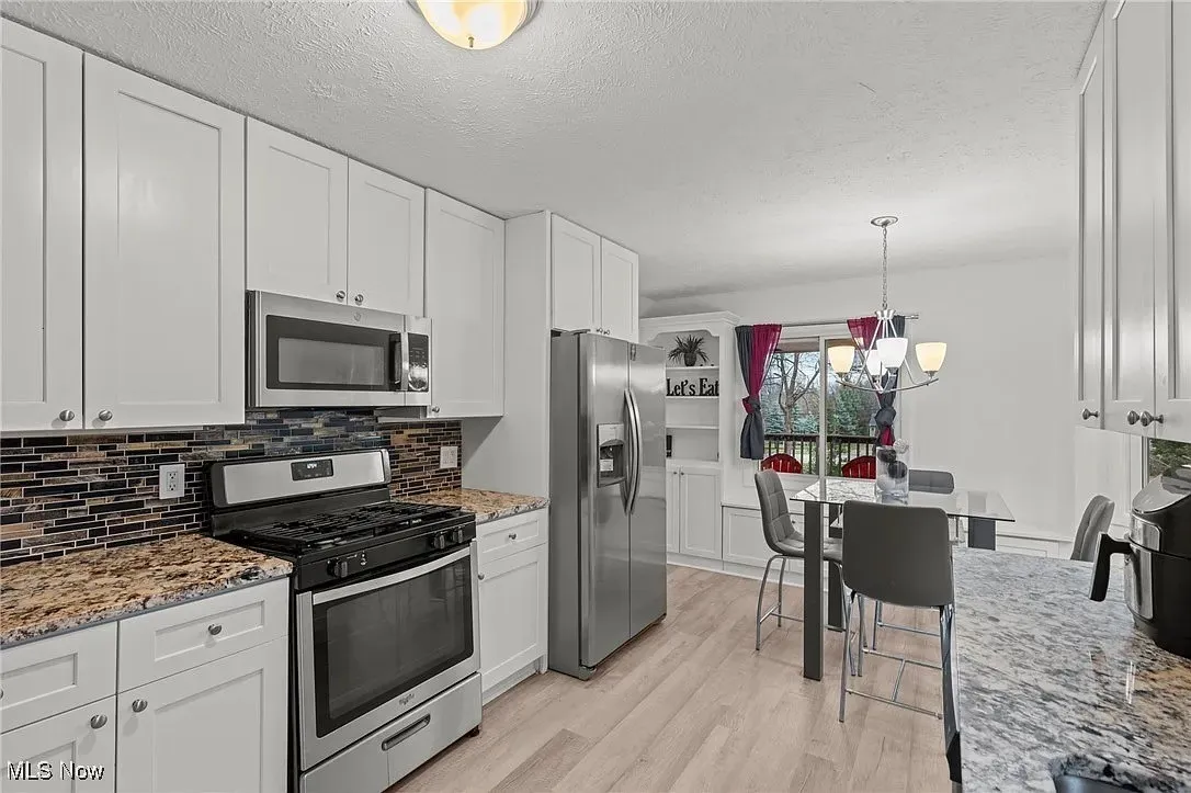 Kitchen featuring appliances with stainless steel finishes, white cabinetry, a chandelier, light wood-type flooring, and backsplash