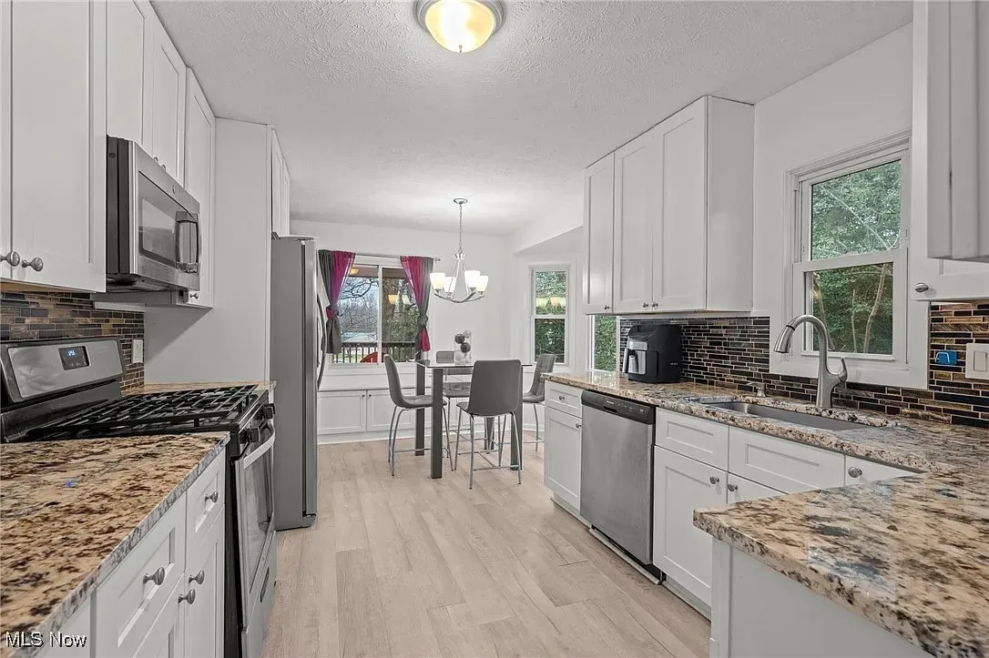 Kitchen with appliances with stainless steel finishes, a chandelier, light wood-style floors, white cabinetry, and a textured ceiling