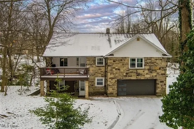 View of front facade featuring stone siding, a garage, a chimney, and dirt driveway