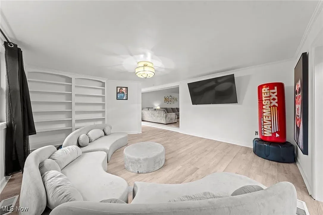 Living room with built in shelves, wood finished floors, and ornamental molding
