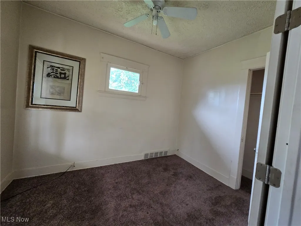 Spare room with dark carpet, a textured ceiling, and ceiling fan