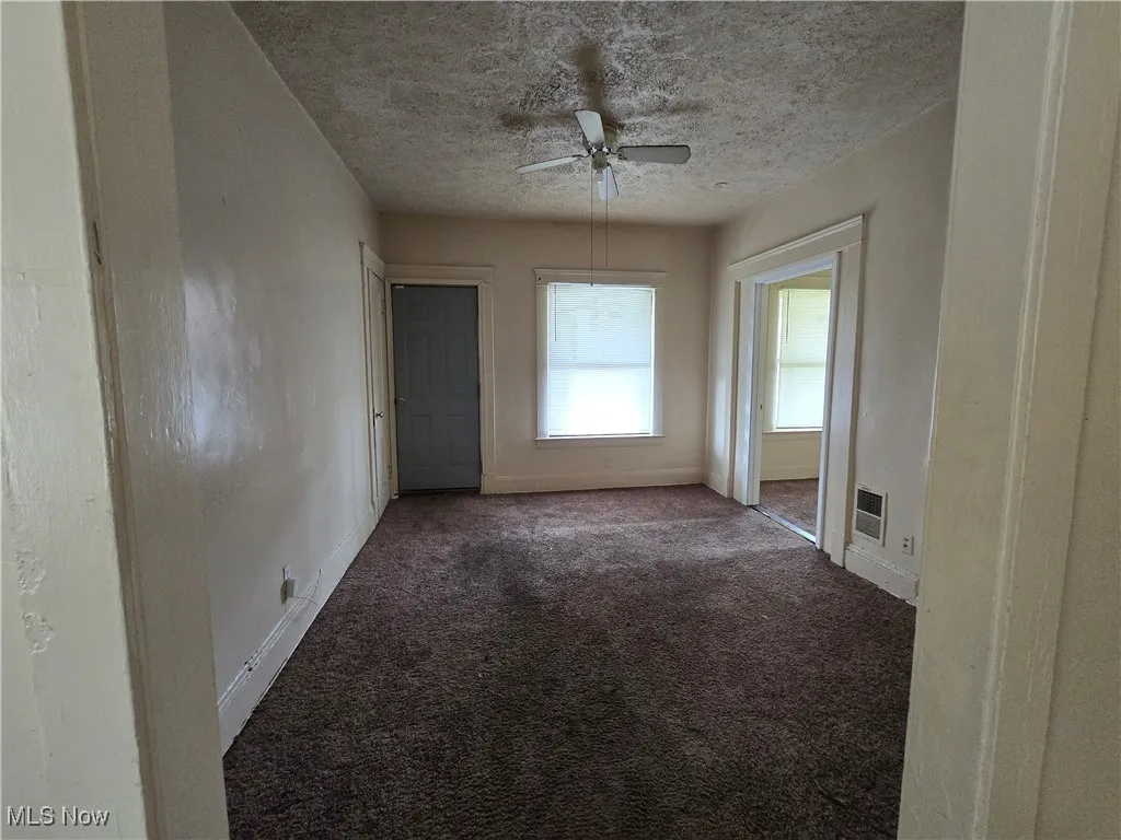 Carpeted empty room with ceiling fan and a textured ceiling