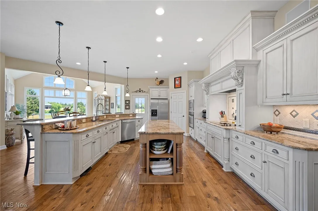 Kitchen featuring stainless steel appliances, open shelves, a large island, recessed lighting, and a breakfast bar