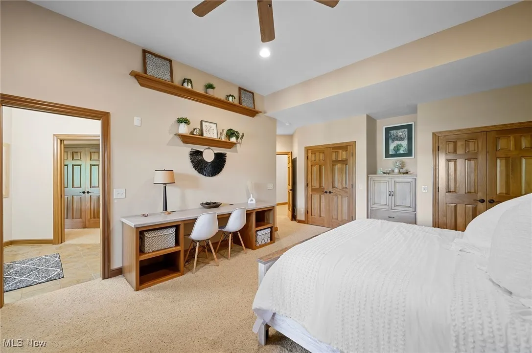 Bedroom with multiple closets, light carpet, connected bathroom, a ceiling fan, and an office area