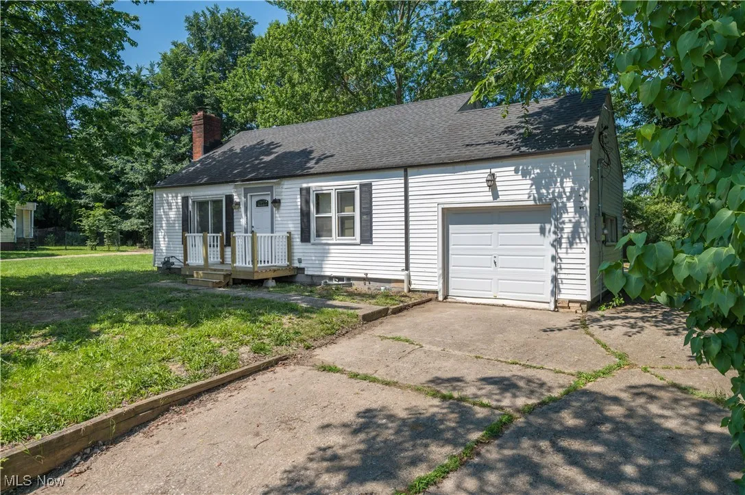 View of front of home featuring an attached garage, concrete driveway, a front yard, a chimney, and roof with shingles
