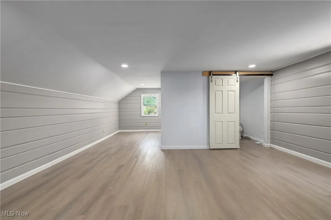 Bonus room with a barn door, wood finished floors, wooden walls, recessed lighting, and lofted ceiling