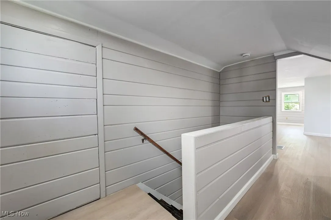Hall with an upstairs landing, wood finished floors, and lofted ceiling