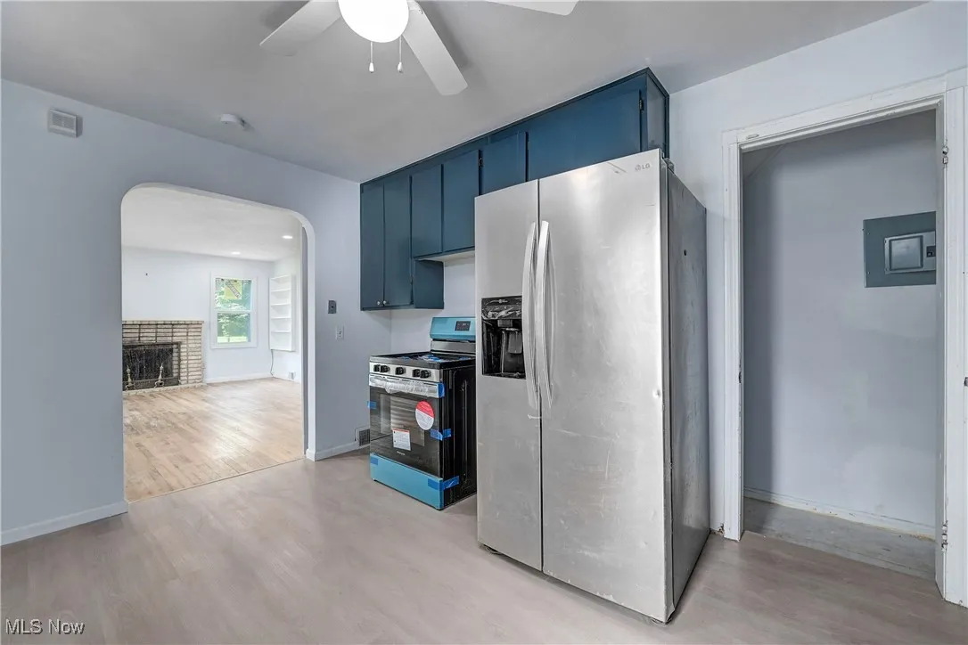 Kitchen with appliances with stainless steel finishes, blue cabinets, light wood-style floors, a ceiling fan, and arched walkways