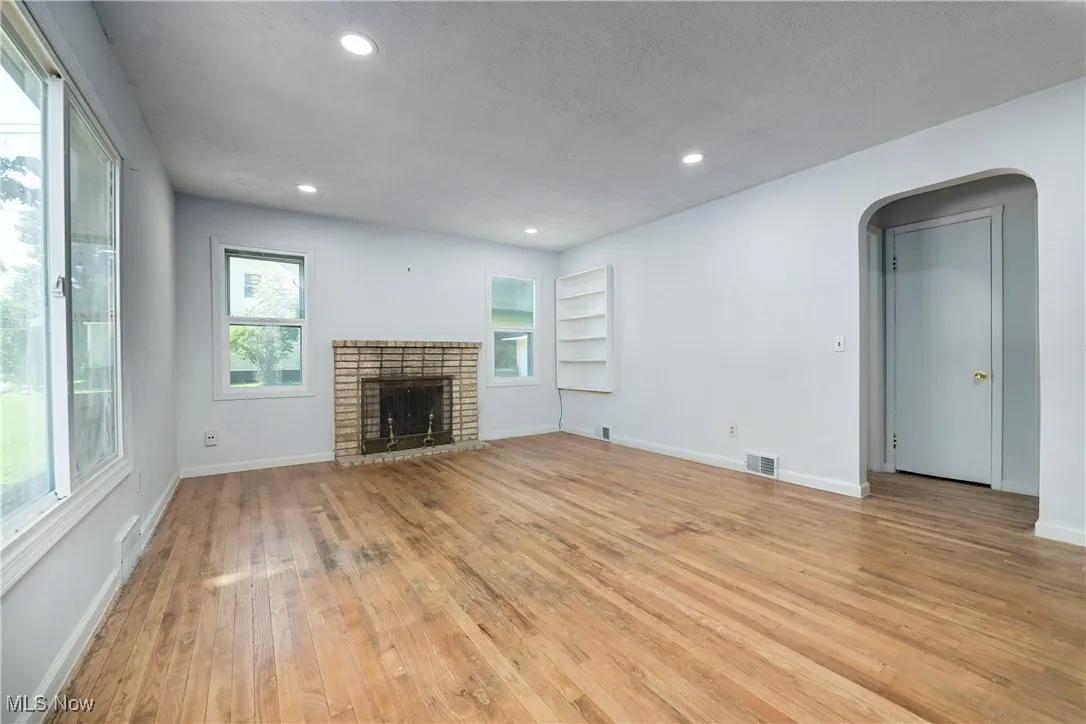 Unfurnished living room featuring light wood-type flooring, arched walkways, a fireplace, recessed lighting, and built in shelves