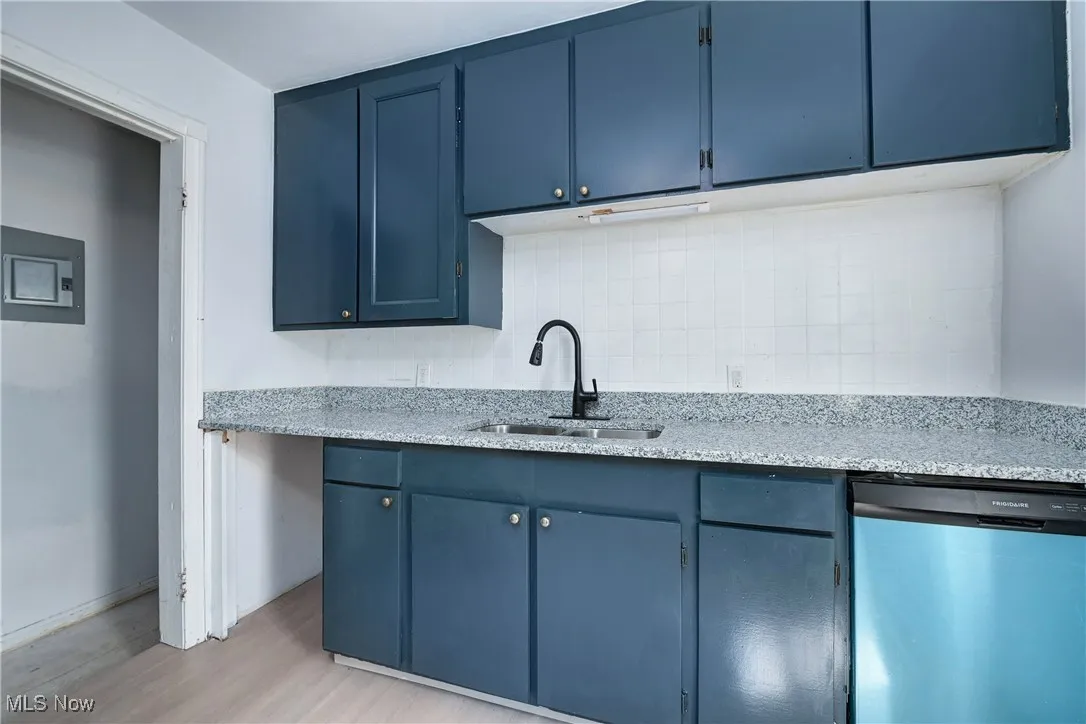 Kitchen with dishwasher, blue cabinets, backsplash, light wood-type flooring, and light stone countertops