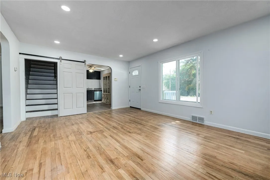 Unfurnished living room featuring arched walkways, light wood-type flooring, stairs, recessed lighting, and a barn door