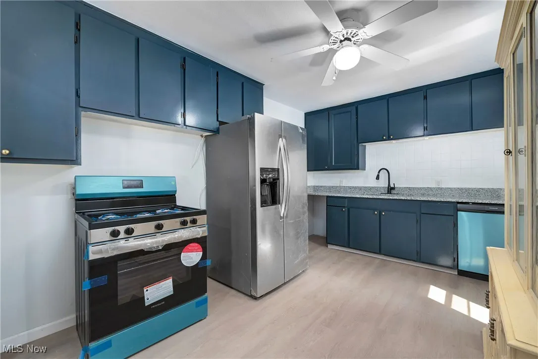 Kitchen with stainless steel appliances, blue cabinetry, light wood-type flooring, and backsplash
