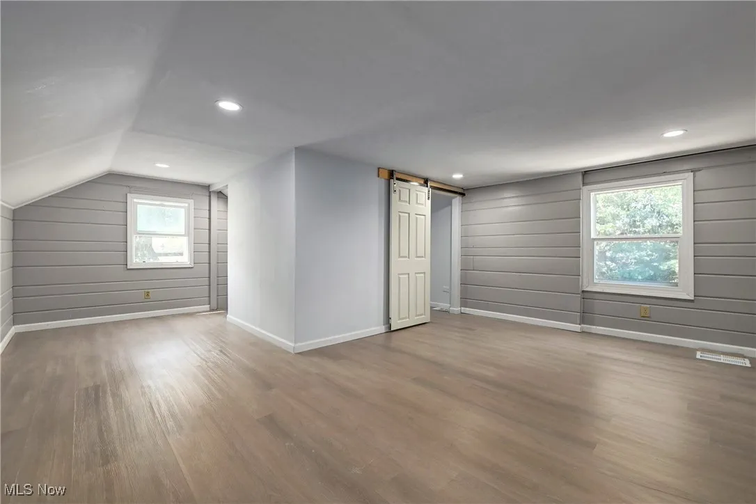 Additional living space featuring a barn door, wood finished floors, vaulted ceiling, recessed lighting, and wooden walls