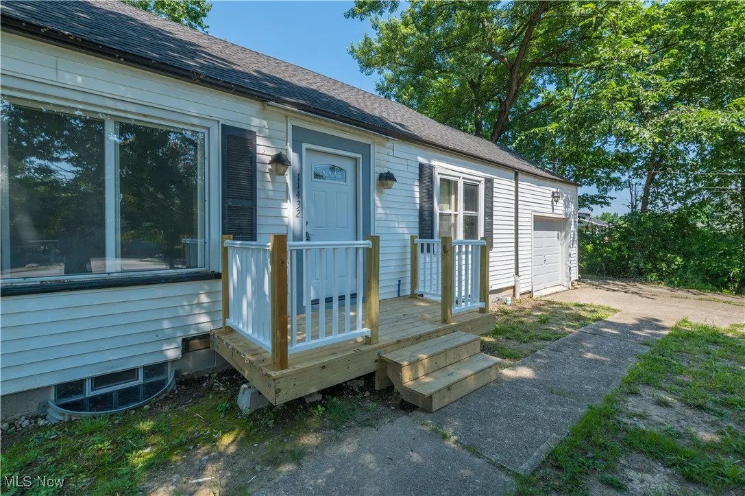 Property entrance with a garage, driveway, a shingled roof, and a deck