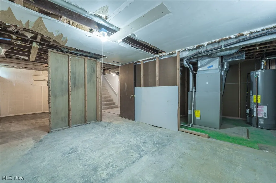 Unfinished below grade area featuring gas water heater, heating unit, and stairs