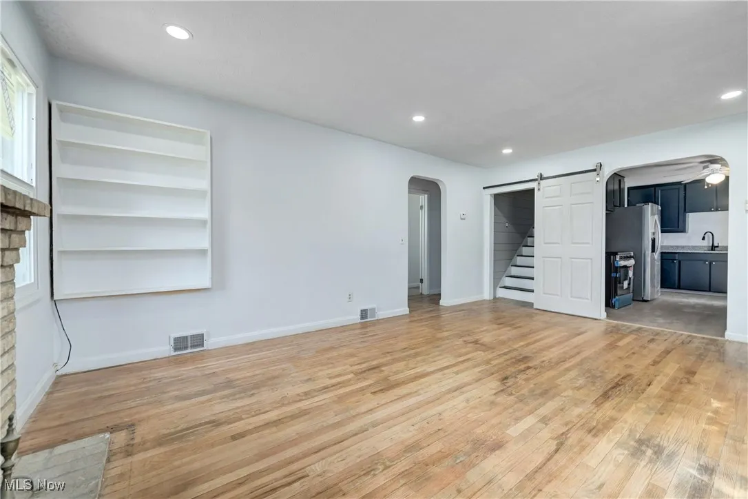 Unfurnished living room with arched walkways, a barn door, light wood-style floors, and recessed lighting
