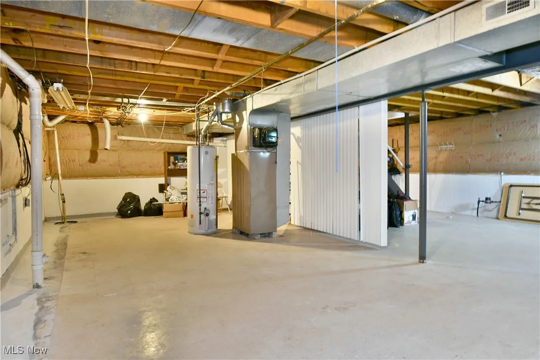 Unfinished below grade area featuring water heater and heating unit