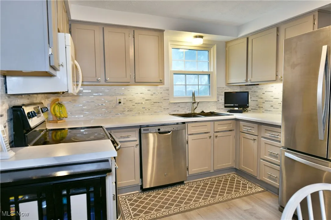 Kitchen featuring stainless steel appliances, light countertops, backsplash, light wood-style flooring, and gray cabinets