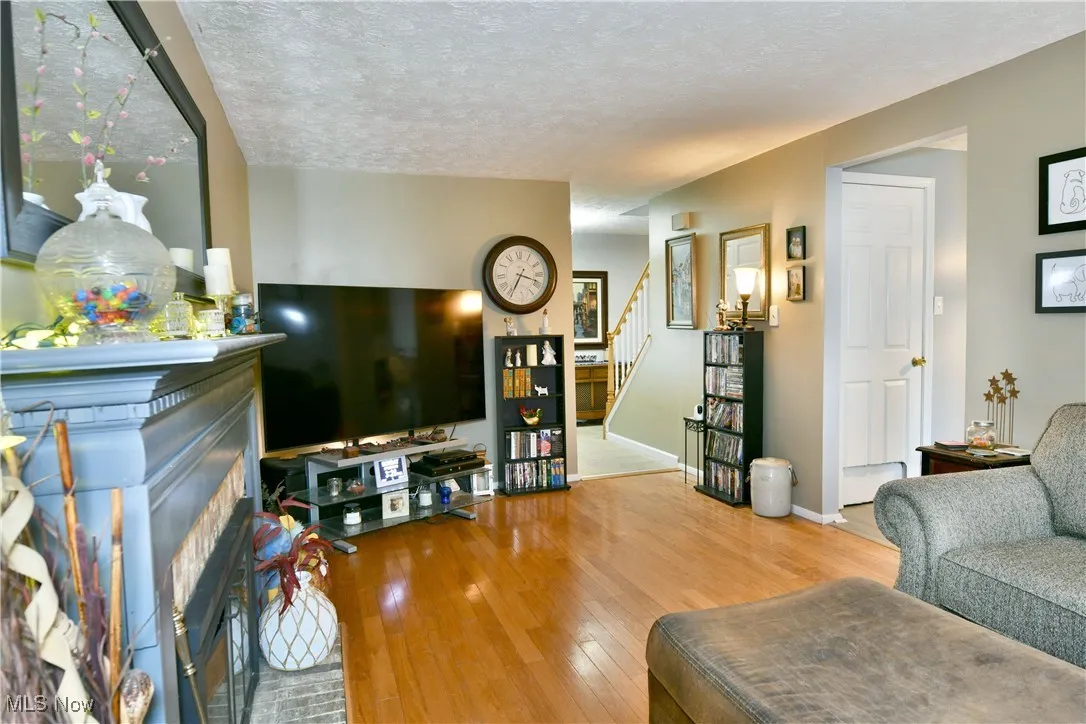 Living area with stairs, a brick fireplace, hardwood / wood-style floors, and a textured ceiling