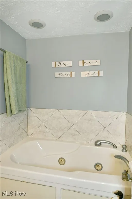 Full bathroom featuring a tub with jets and a textured ceiling