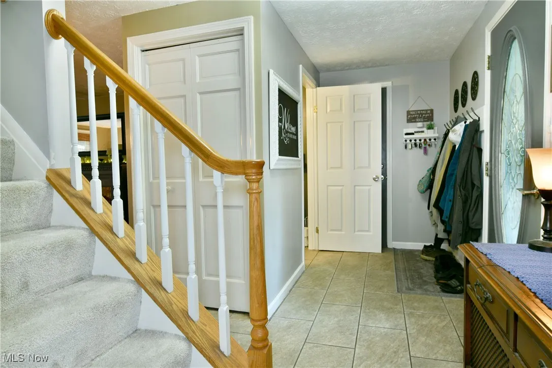 Foyer featuring stairs, light tile patterned floors, and a textured ceiling