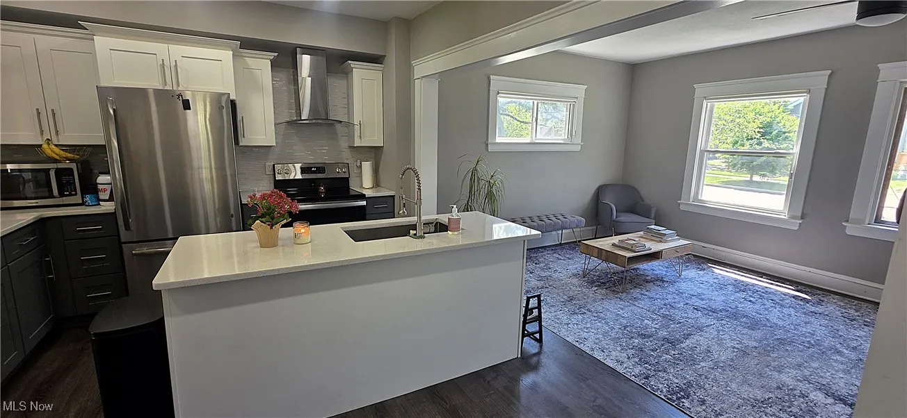 Kitchen featuring stainless steel appliances, wall chimney range hood, dark wood finished floors, light countertops, and backsplash