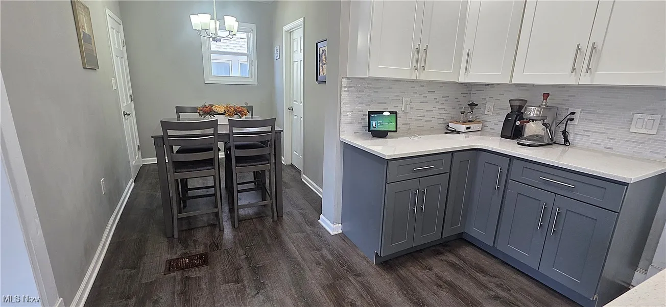 Kitchen with dark wood-style floors, gray cabinetry, backsplash, and a chandelier