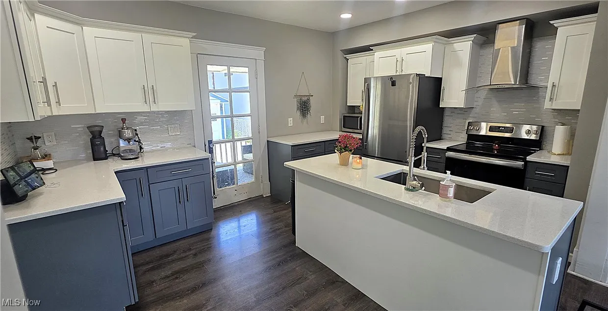 Kitchen with wall chimney exhaust hood, stainless steel appliances, dark wood finished floors, decorative backsplash, and recessed lighting