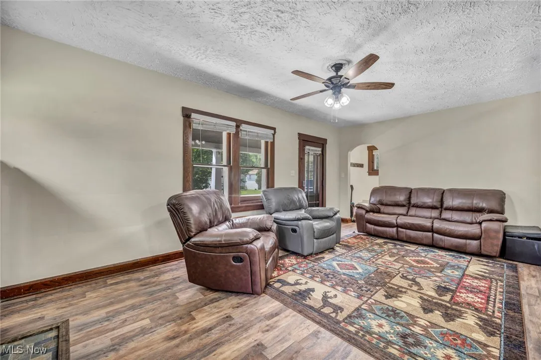 Living room with arched walkways, wood finished floors, ceiling fan, and a textured ceiling