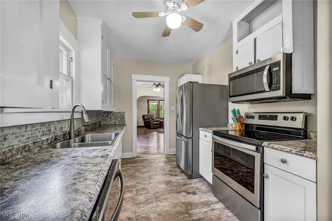 Kitchen with stainless steel appliances, ceiling fan, tasteful backsplash, white cabinetry, and arched walkways