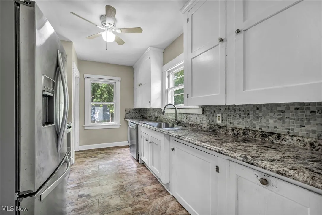 Kitchen featuring stainless steel appliances, decorative backsplash, white cabinets, stone finish flooring, and a ceiling fan