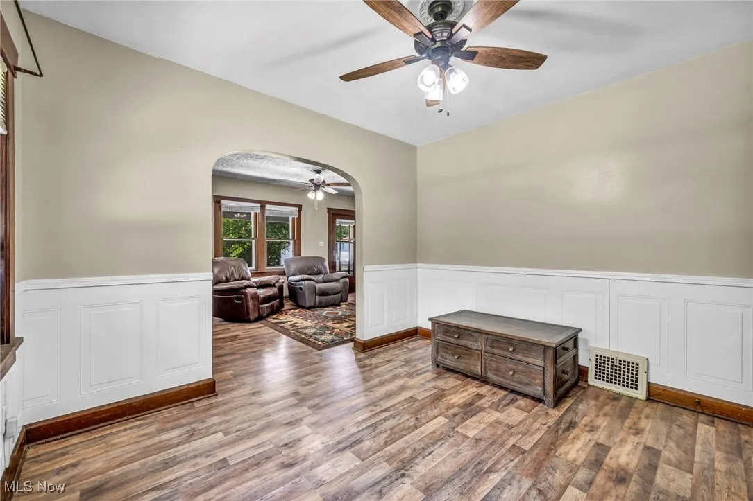 Spare room with arched walkways, a ceiling fan, a wainscoted wall, wood finished floors, and a decorative wall