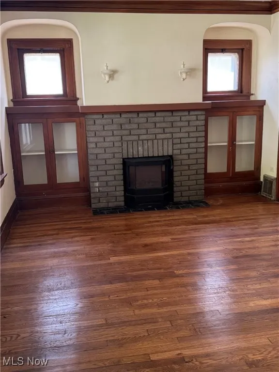 Unfurnished living room with dark wood-style flooring and a brick fireplace