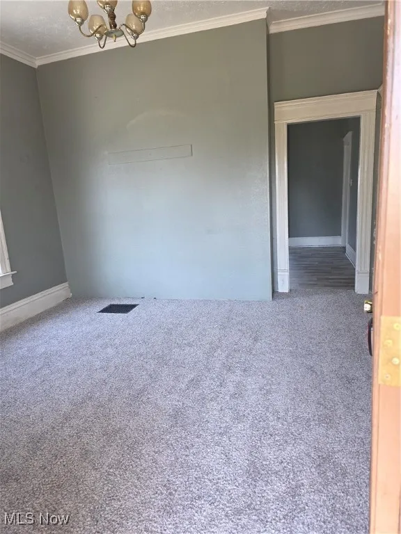 Spare room featuring a chandelier, carpet, and crown molding