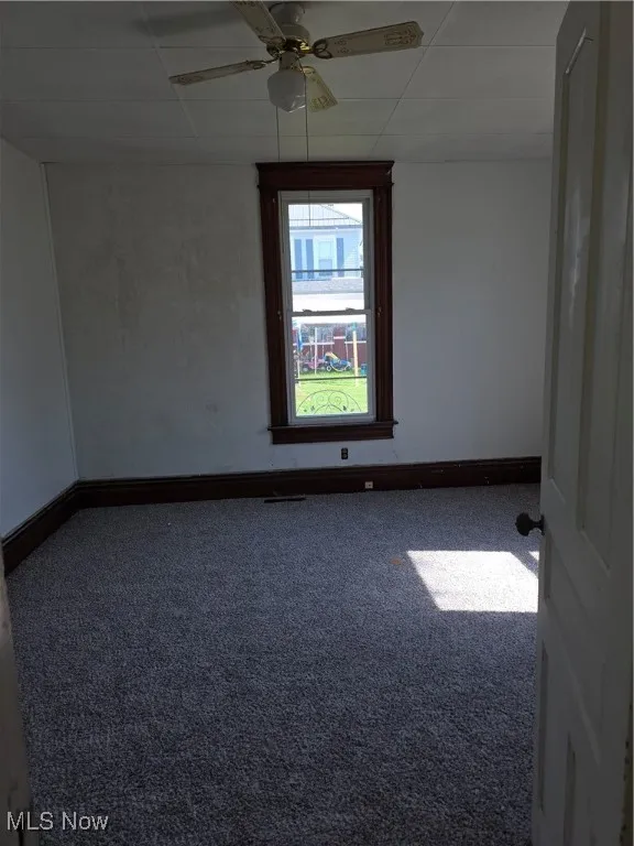 Carpeted spare room featuring a drop ceiling and ceiling fan