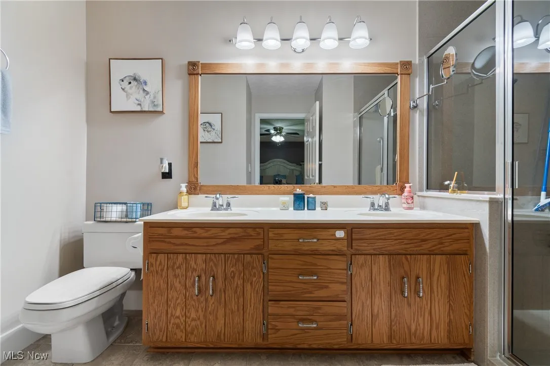 Full bath featuring double vanity, a stall shower, and ceiling fan